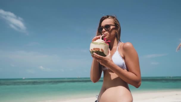 Женщина пьет свежую кокосовую воду с соломой на пляже — стоковое видео