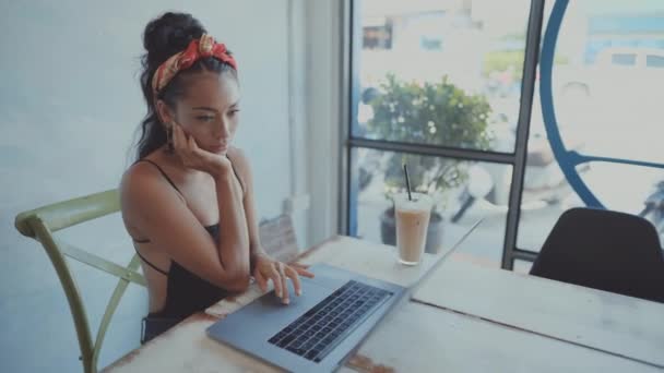 Menina asiática bonita trabalhando em um café com um laptop. freelancer feminino trabalhando em cafeteria — Vídeo de Stock