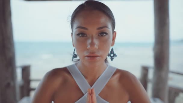 Woman looking straight at camera and meditating under villa near ocean — Stock Video