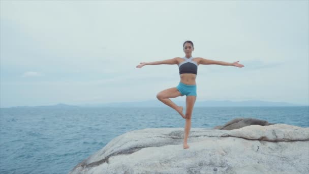 Kvinna stående på ett ben och mediterar på klippor nära Ocean — Stockvideo