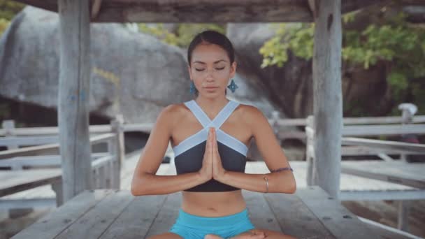 Mujer mirando directamente a la cámara y meditando bajo la villa cerca del océano — Vídeos de Stock