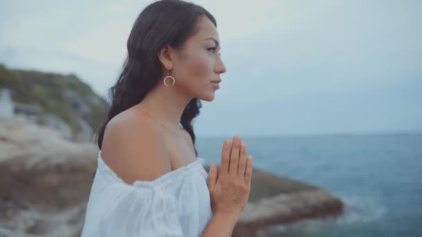 Woman holding her hands together by the ocean and closing her eyes — Stock Video