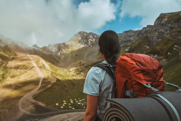 Пішохід з червоним рюкзаком стоїть на вершині гори і насолоджується видом на кемпінгову долину — стокове фото