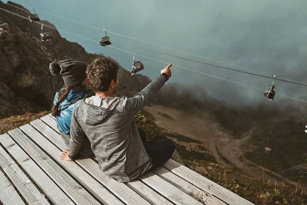 Mladí turisté sedí vysoko v horách, objímají se a dívají se na mraky — Stock fotografie