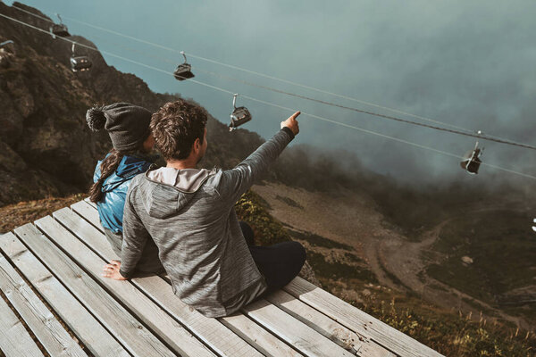 A young hikers sitting high in the mountains hugging and looking at the clouds
