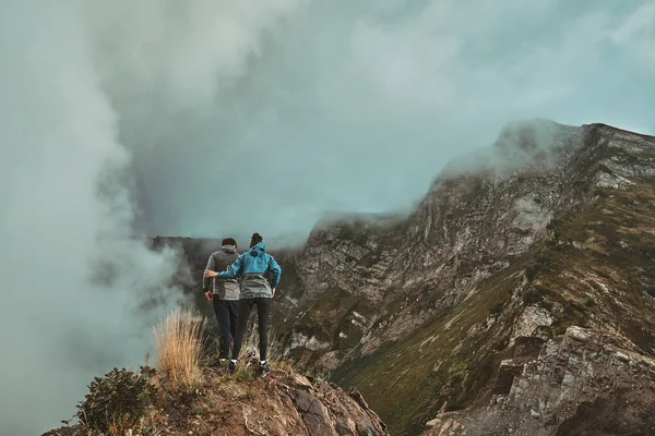 Mladý pár stojící na útesu v horách a dívající se dolů — Stock fotografie