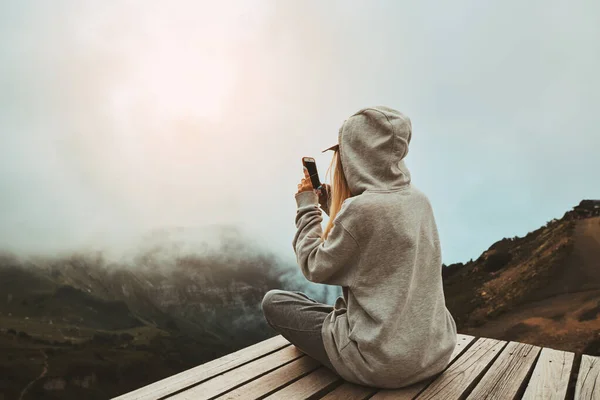 Dívka v šedé mikině sedící na vyhlídce a fotit na chytrém telefonu — Stock fotografie