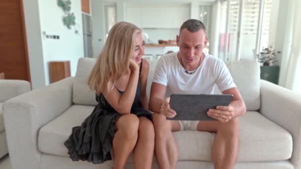 Pareja usando una tableta y sentada en el sofá — Vídeos de Stock