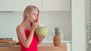 Mutfakta elinde hindistan cevizi olan mutlu genç bir kadın.