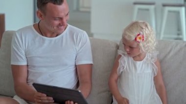 Baba ve kızı kanepede oturup tablet kullanıyorlar.