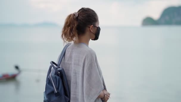 Mladá žena nosí ochrannou masku obličeje na vyhlídce u moře — Stock video
