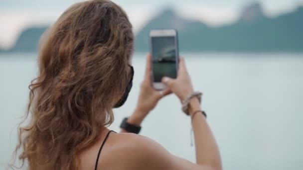 Young woman wearing protective face mask at viewpoint near the sea — Stock Video