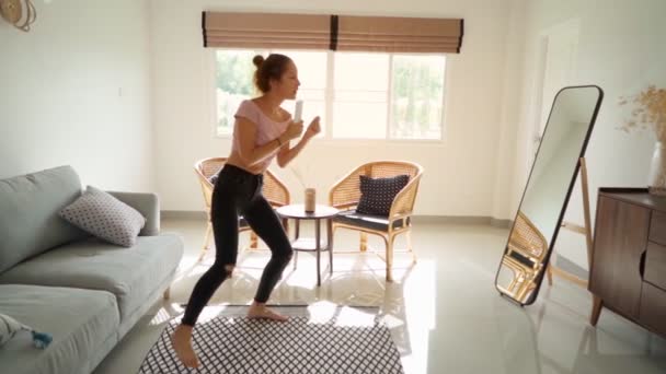 Mujer feliz bailando y cantando en el mando a distancia frente al espejo. divertirse disfrutando de la danza juguetona — Vídeos de Stock