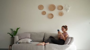 Genç bir kadın koltukta otururken akıllı telefon mesajları yazarken sinirlenir.