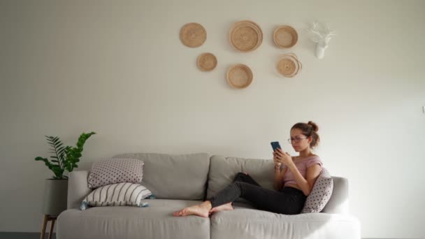 Νεαρή γυναίκα θυμώνουν κατά τη χρήση smart phone γραπτών μηνυμάτων κάθεται στον καναπέ — Αρχείο Βίντεο