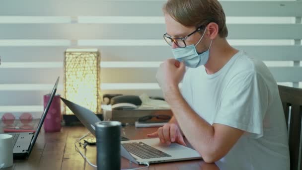 Seorang pria mengenakan topeng pelindung duduk di meja di kafe dengan laptop — Stok Video