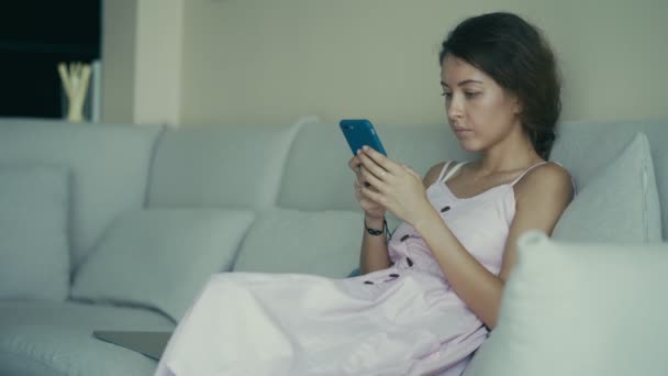 Giovane donna che utilizza smart phone navigare sui social media, controllare le notizie, giocare a giochi per cellulare o messaggi di testo seduti sul divano — Video Stock