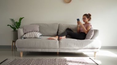 Genç bir kadın koltukta otururken akıllı telefon mesajları yazarken sinirlenir.