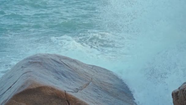 Kraftfulla havsvågor plaskar över en stor klippa i havet. våldsam brytande våg skummande över en klippa nära stenig tropisk strand — Stockvideo