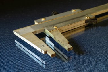 Calliper, siyah arka plandaki cam masanın üzerinde duruyor. Detayların tam ölçümü için bir araç.