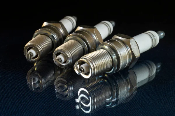 Siyah arka plandaki arabanın bujisi. Ayrıntılar cam masaya yansıtılıyor.