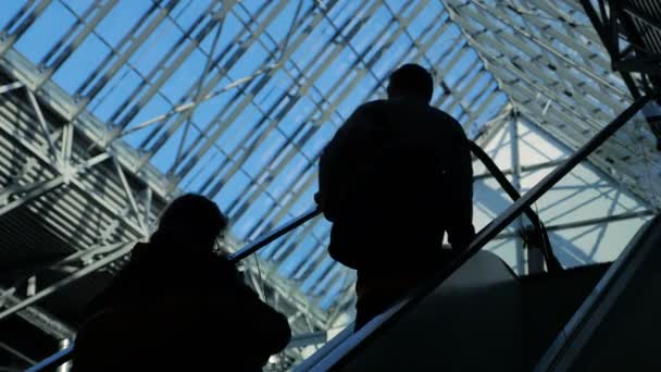 Люди силуети на ескалаторі рухаються у бізнес-центрі з великими вікнами — стокове відео