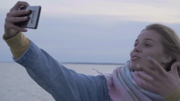 Молодая женщина делает селфи на осеннем пляже по телефону — стоковое видео