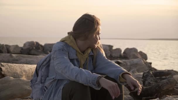 Chica infeliz sentada en la playa mira al atardecer — Vídeos de Stock