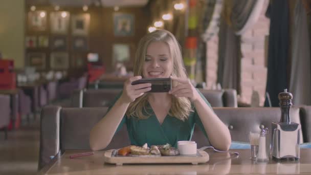 Lachende vrouw maken een foto van steak in restaurant — Stockvideo