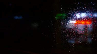 Bulanık yağmur damlaları arabanın camına ve gece ışıklarına düşer