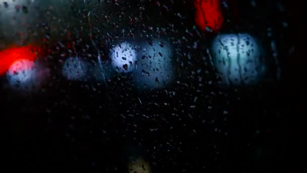 ビュー アベニューに移動の車の中で夜の秋市道路上の輸送の概念 雨の中で自動車のウィンドウを削除します カラフルなライトと抽象的な背景をぼかした写真 — ストック動画