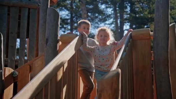 Niños abrazos en el campo parque infantil tobogán de madera — Vídeo de stock