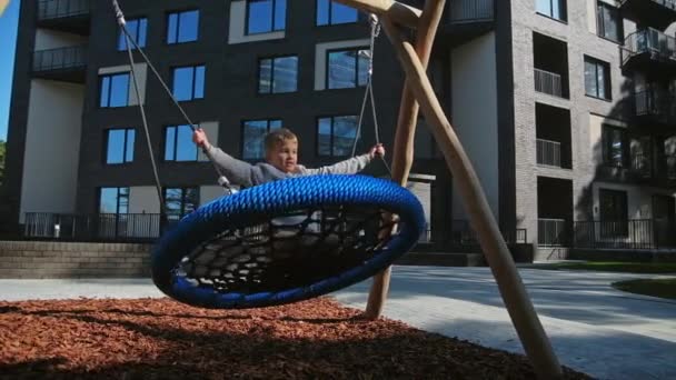 Child boy swinging in urban playground slow motion — Stock Video