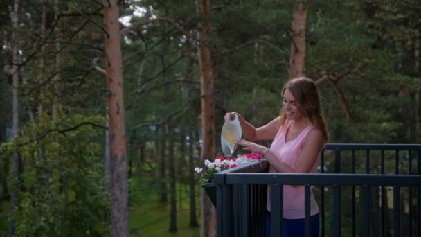 Женщина поливает цветы на балконе загородного дома — стоковое видео