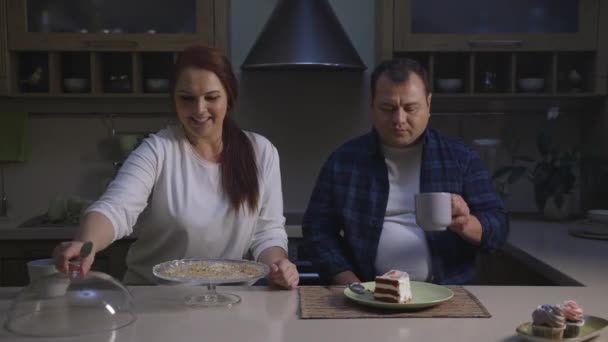 Забавная кавказская семья, стоящая рядом со столом и заканчивающая праздничный торт — стоковое видео