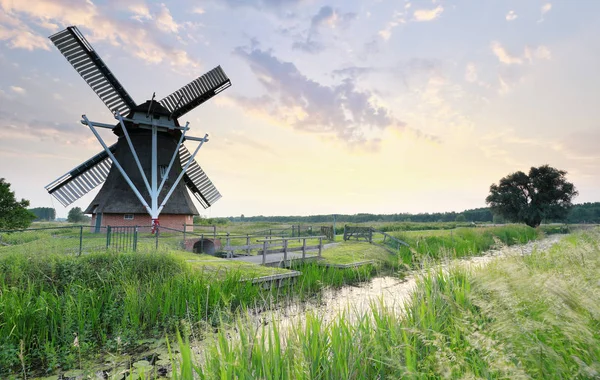 Moinho de vento holandês por rio ao pôr do sol — Fotografia de Stock