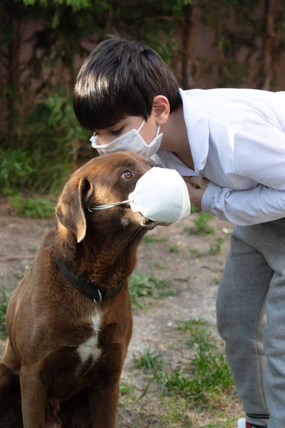 Niño con una máscara protectora con un perro debido a la pandemia del virus de la corona covid-19 —  Fotos de Stock