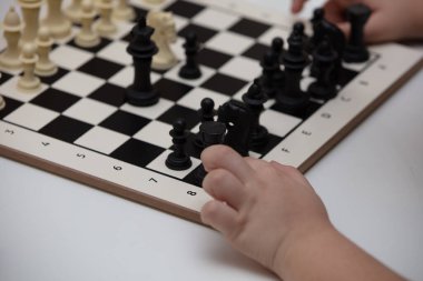 Bir masada oturur ve satranç oynar. Çocuk oyuna konsantre oldu. 