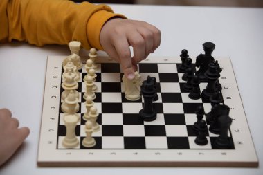 Bir masada oturur ve satranç oynar. Çocuk oyuna konsantre oldu. 