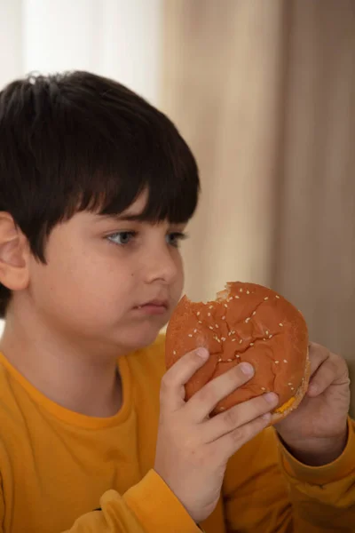 Cute healthy preschool kid boy eats hamburger sitting in school or nursery cafe. — Stock Photo, Image