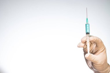 Beyaz arka planda ilaç içeren bir şırınga tutan lateks eldiven.