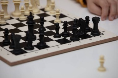 Bir masada oturur ve satranç oynar. Çocuk oyuna konsantre oldu ve bir sonraki hamlesini nerede yapacağını düşündü. Erken gelişim, çocuklar için evde eğitim oyunları