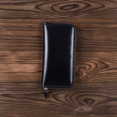 Ahşap desenli arka planda parlak siyah el yapımı deri porte-monnaie. Görüş açımız düşük. Lüks aksesuarların stok fotoğrafı.