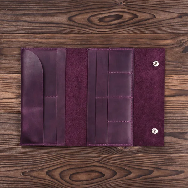 Purple handmade travel wallet lies on textured wooden backgroud closeup. Wallet is open and empty. Up to down view. Stock photo of businessman accessories.