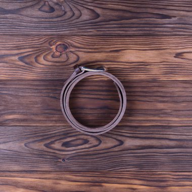 Kahverengi renkli el yapımı kemer desenli ahşap arka planda yatar. Kemer halka şeklinde bükülmüş. Görüş açımız düşük. İşadamı aksesuarlarının resmi.. 