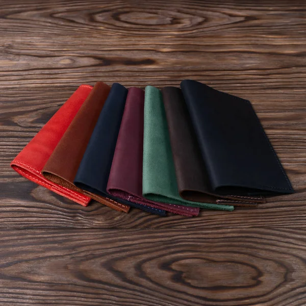 Six handmade leather passport covers on wooden textured background. Stock photo of luxury accessories.