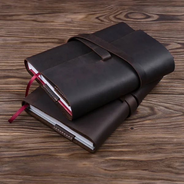 Two brown handmade leather notebook cover with notebook inside on wooden background. Stock photo of luxury business accessories.