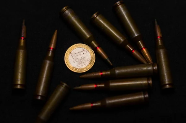 ブラックを背景に1ユーロ硬貨付近のライフル弾 お金のための戦争と世界の問題の一つを象徴する — ストック写真