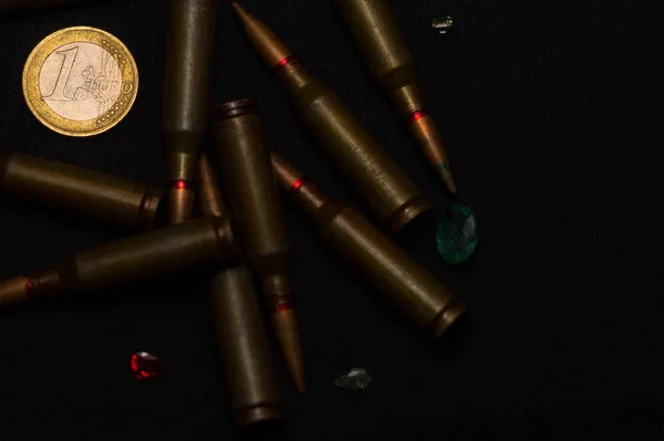 ブラックを背景に1ユーロ硬貨の重さの宝石の周りのライフル弾 お金のための戦争と世界の問題の一つを象徴する — ストック写真