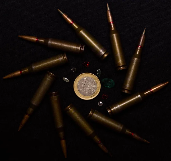 ブラックを背景に1ユーロ硬貨の周りに宝石がたくさんあるライフルの弾薬 お金のための戦争と世界の問題の一つを象徴する — ストック写真